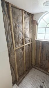 Rebuilding bathroom wall with new 2x4 framing and insulation during Orlando Airbnb shower remodel by Cornerstone Flooring